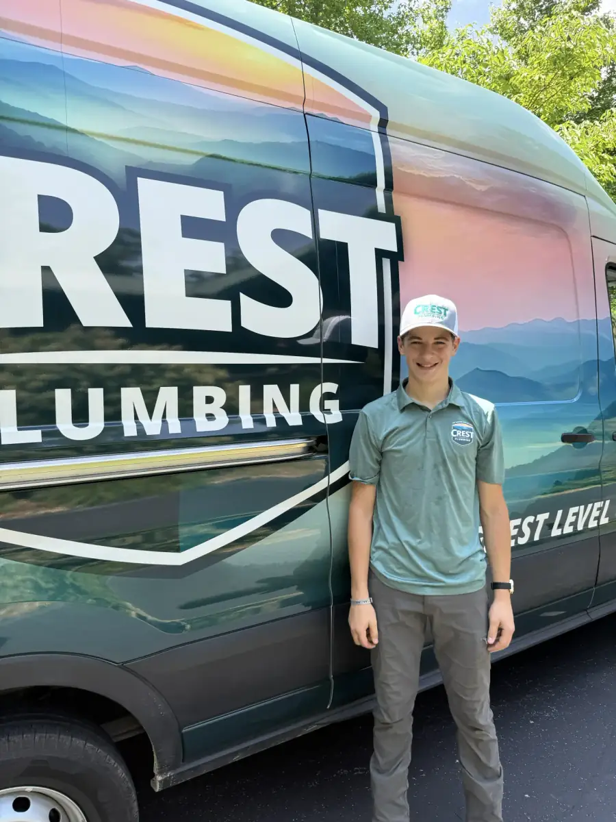 A Crest Plumbing apprentice standing beside a branded Crest Plumbing service van in Cookeville, Tennessee