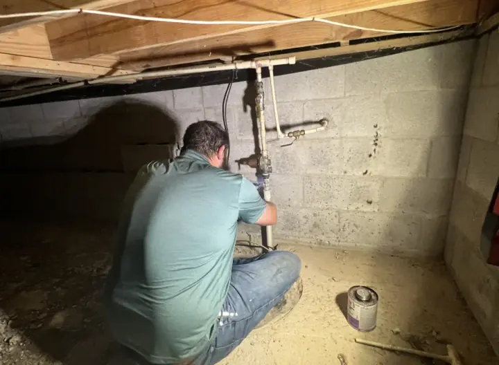 Crest Plumbing technician working on water piping under a home